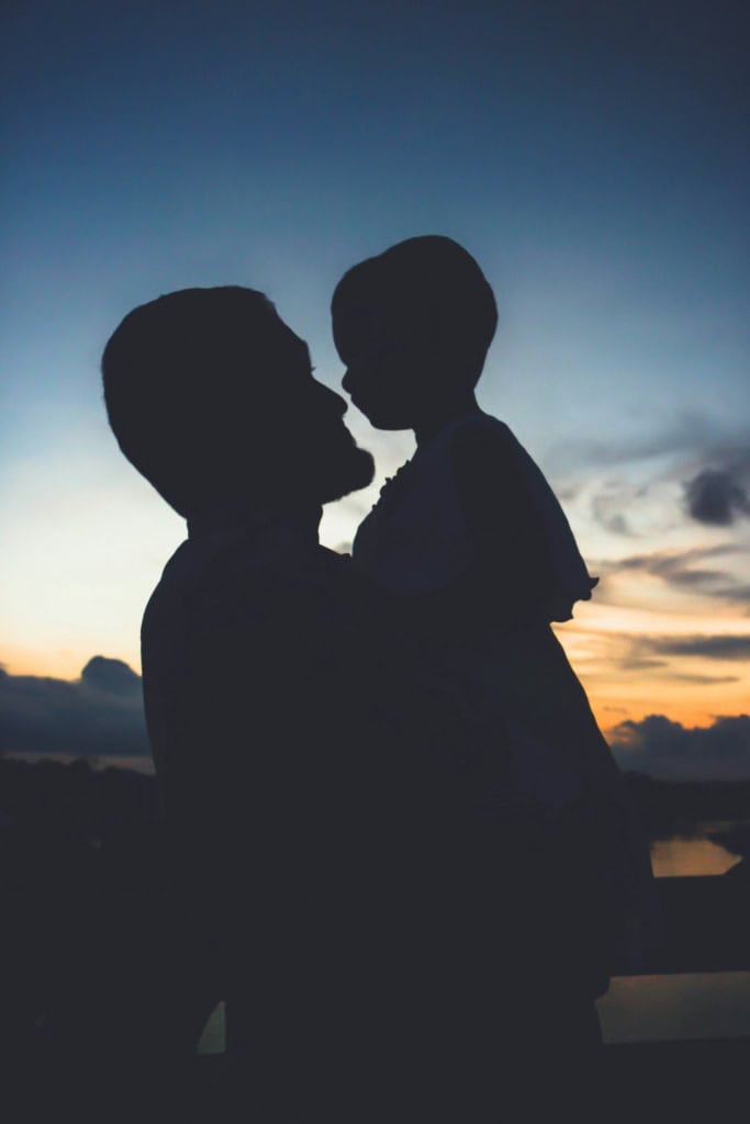 Silhouetted man holding a child against a blue sunset sky